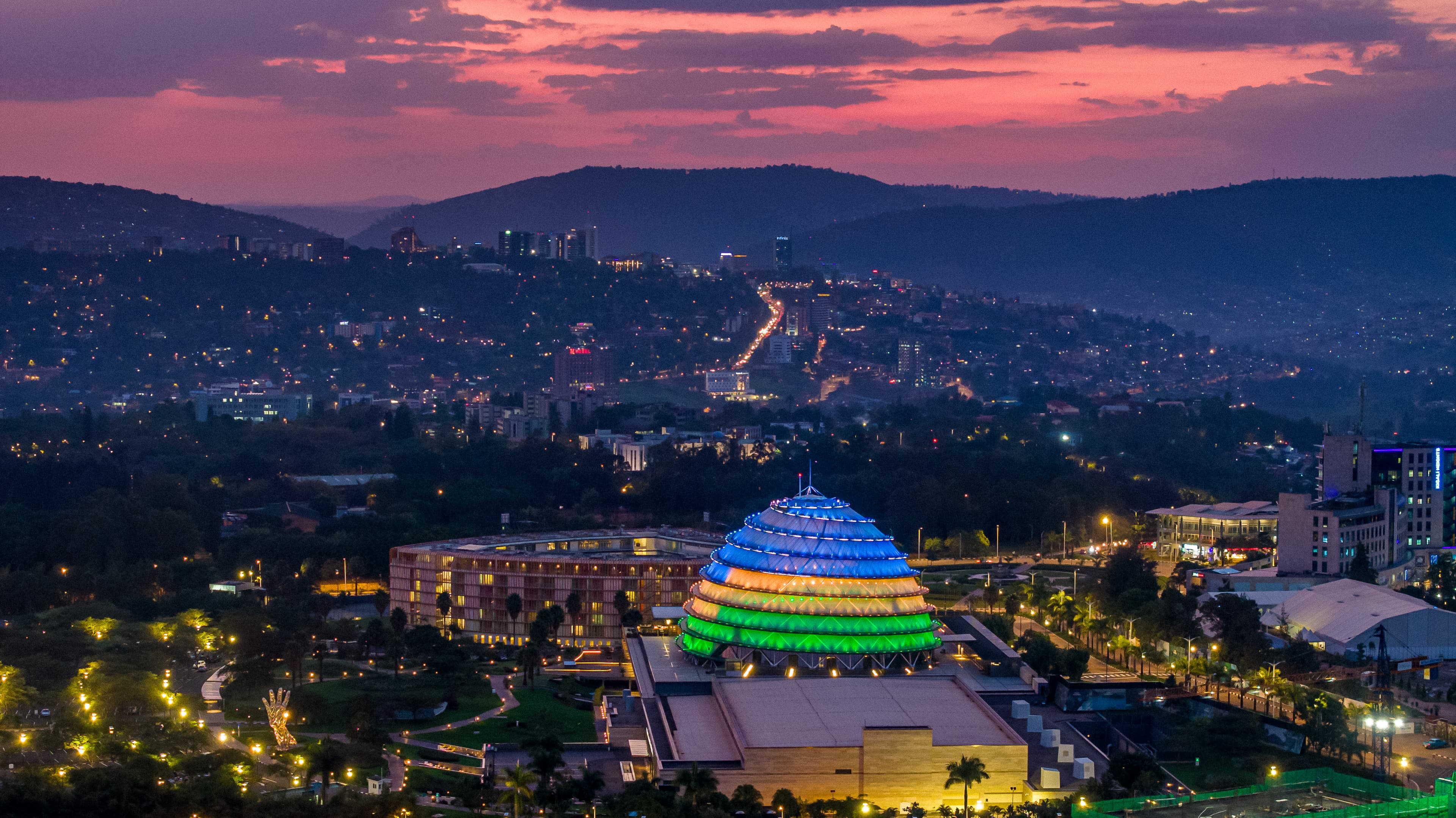 The Kigali Convention Centre lit in Rwanda's colours at dusk, above the city and hills