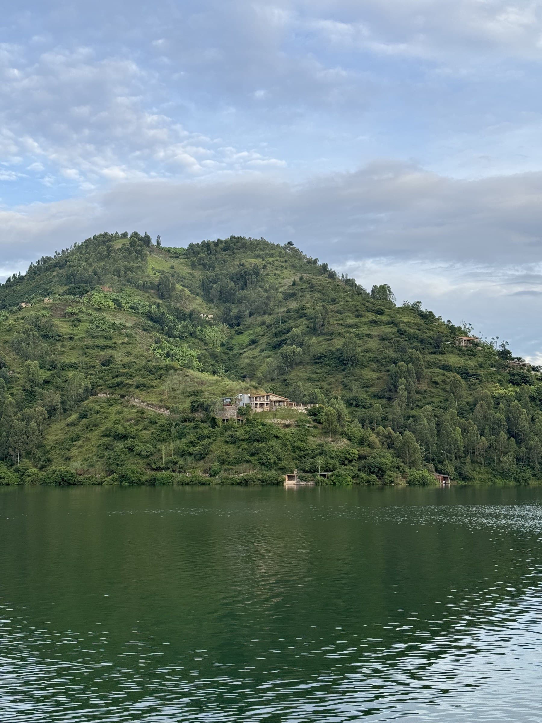Une maison au bord d’un lac, sur une colline verdoyante du Rwanda, au-dessus d’eaux calmes, au crépuscule